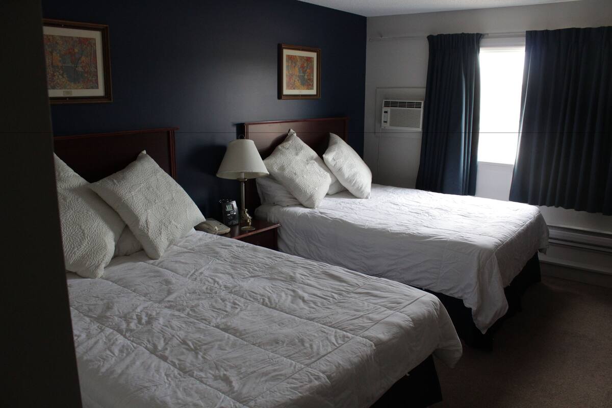 A hotel room with two beds, a nightstand with a lamp, and artwork on the walls.