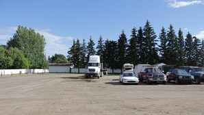 A parking lot with several vehicles, including a white truck, a red truck, and a white car. - Morinville Plaza & Suites (Morinville)