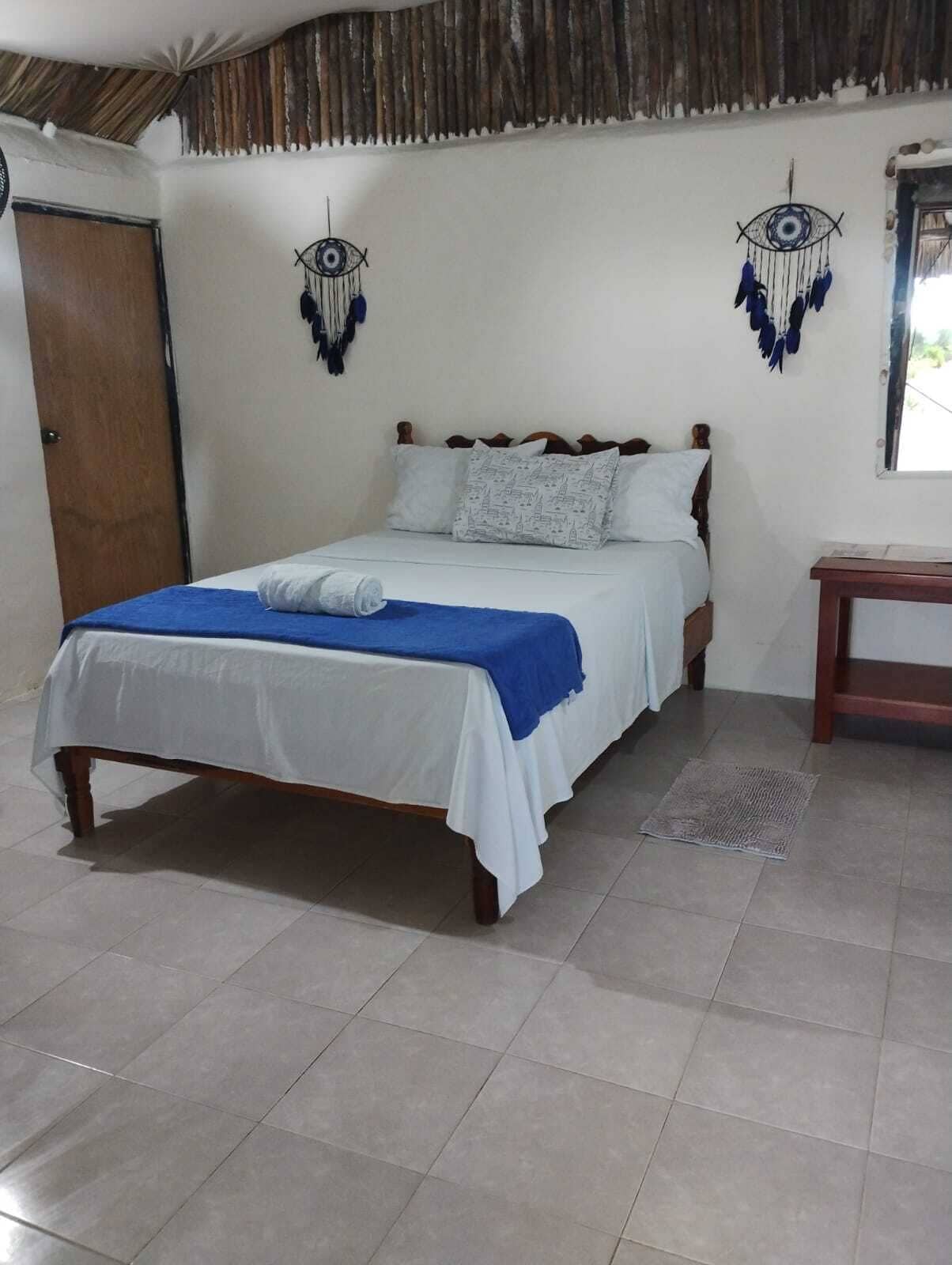 Ein Einzelbett mit weißblauer Bettdecke, einem hölzernen Kopfteil und einem kleinen Nachttisch daneben.