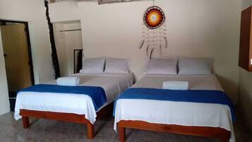A room with two beds, each with a white and blue bedspread, a dreamcatcher on the wall, and a wooden bench.