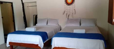 A room with two beds, each with a white and blue bedspread, a dreamcatcher on the wall, and a wooden bench.