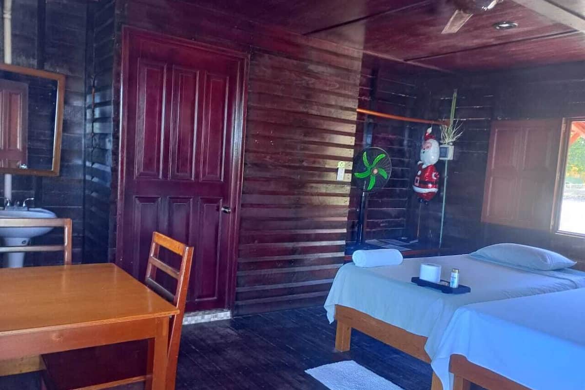 A wooden cabin-style room with a wooden table, two beds, a mirror, and a window.