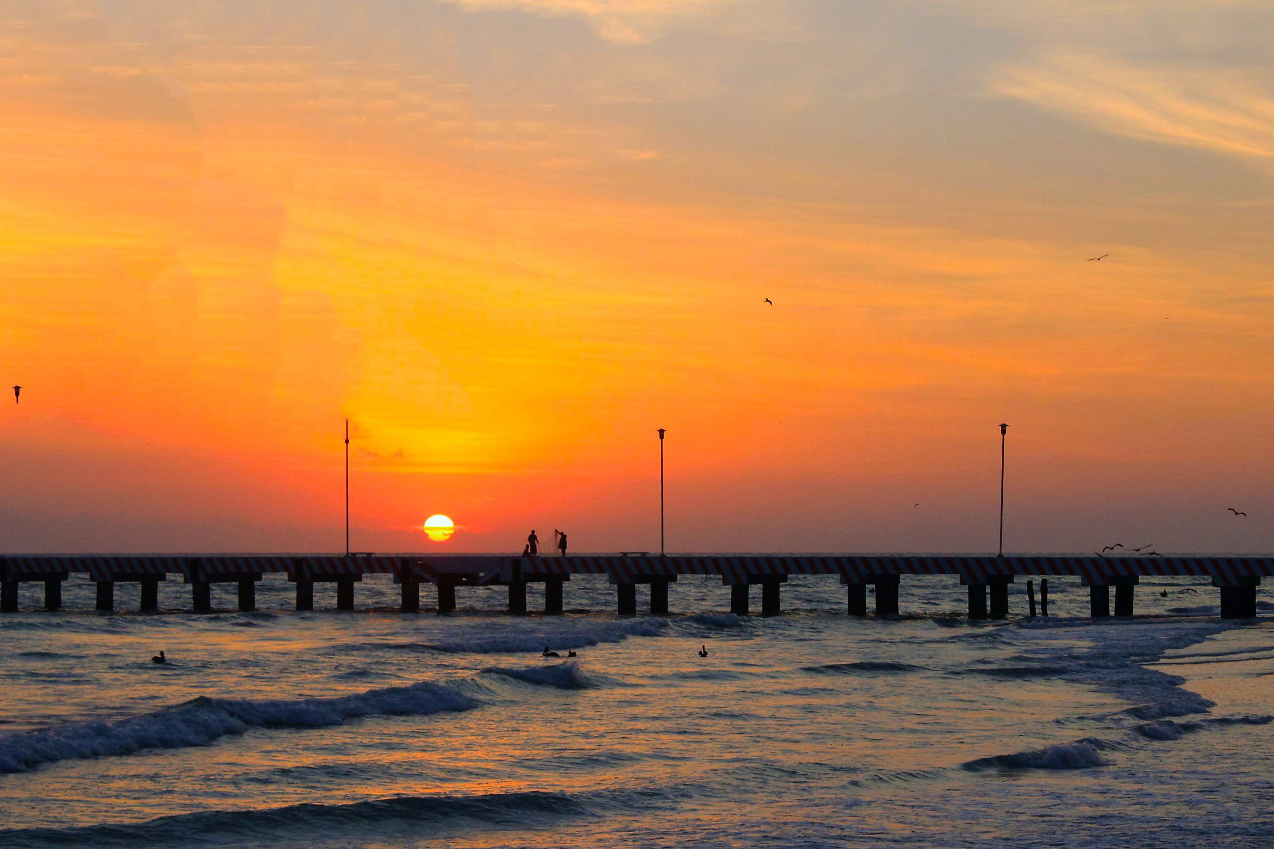 A pier extending into the ocean at sunset with the sun setting in the background.