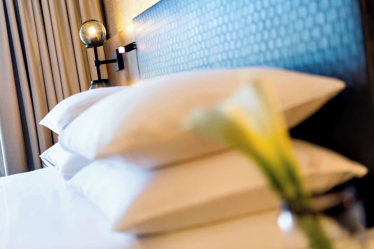 Une chambre d’hôtel avec un lit, des oreillers, une lampe de chevet et un mur orné d’un motif texturé.