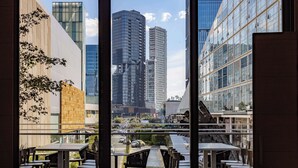 An outdoor dining area with tables and chairs, overlooking a cityscape with modern buildings and a clear sky.