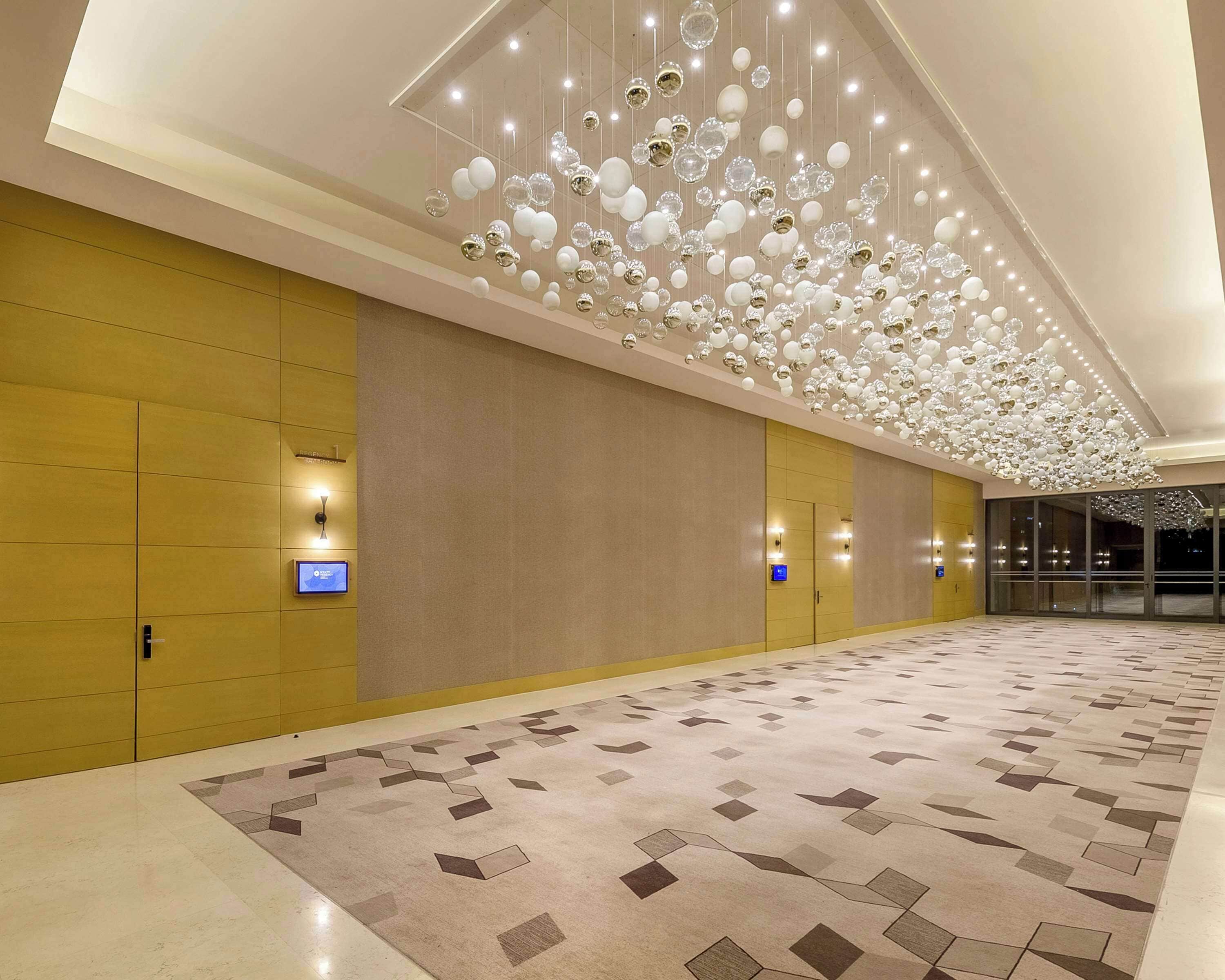 Un pasillo amplio con alfombra estampada, iluminación empotrada y un techo decorado con esferas colgantes.