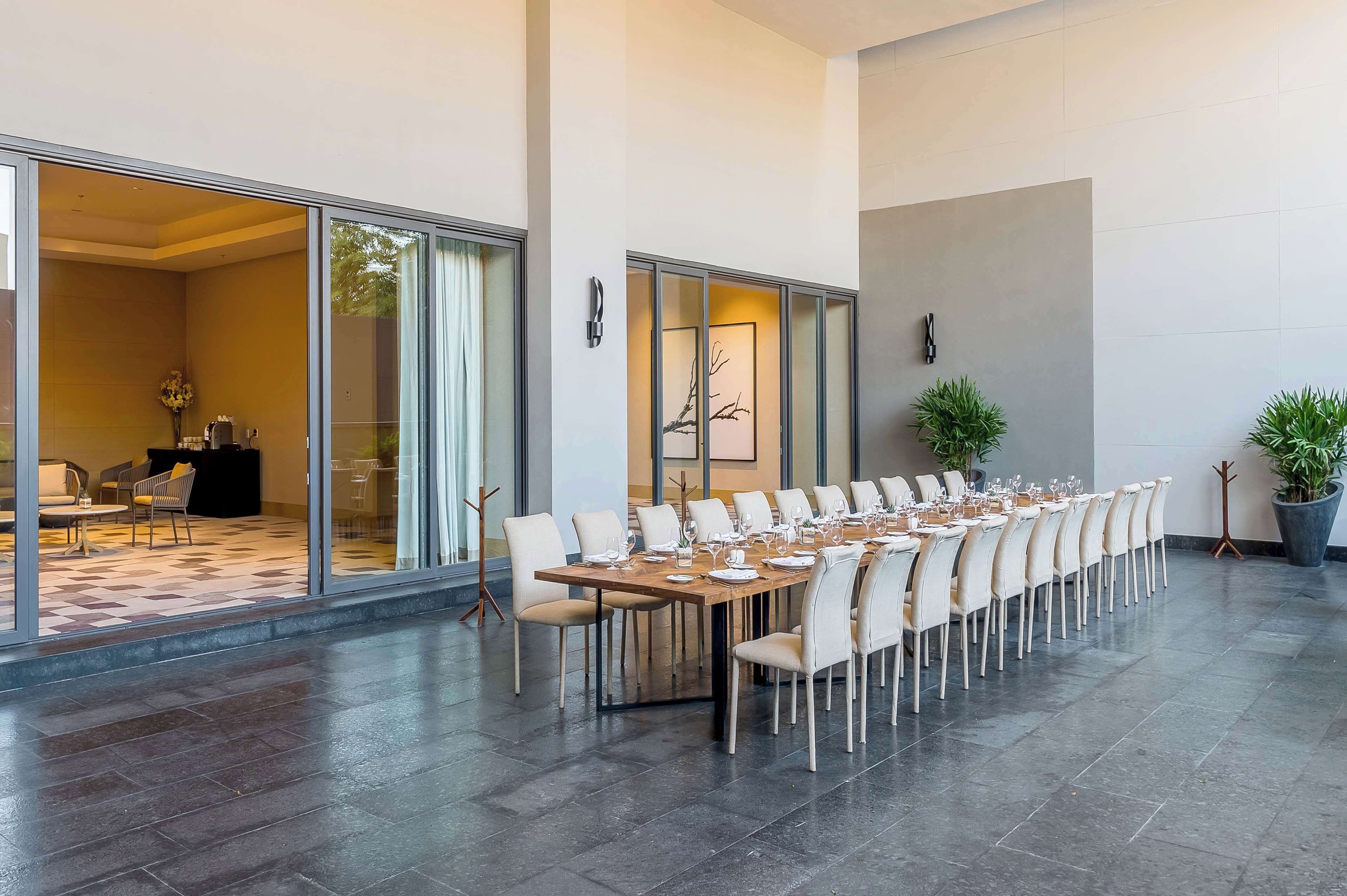 A spacious dining area with a long table set for a meal, large windows, and a modern interior design.