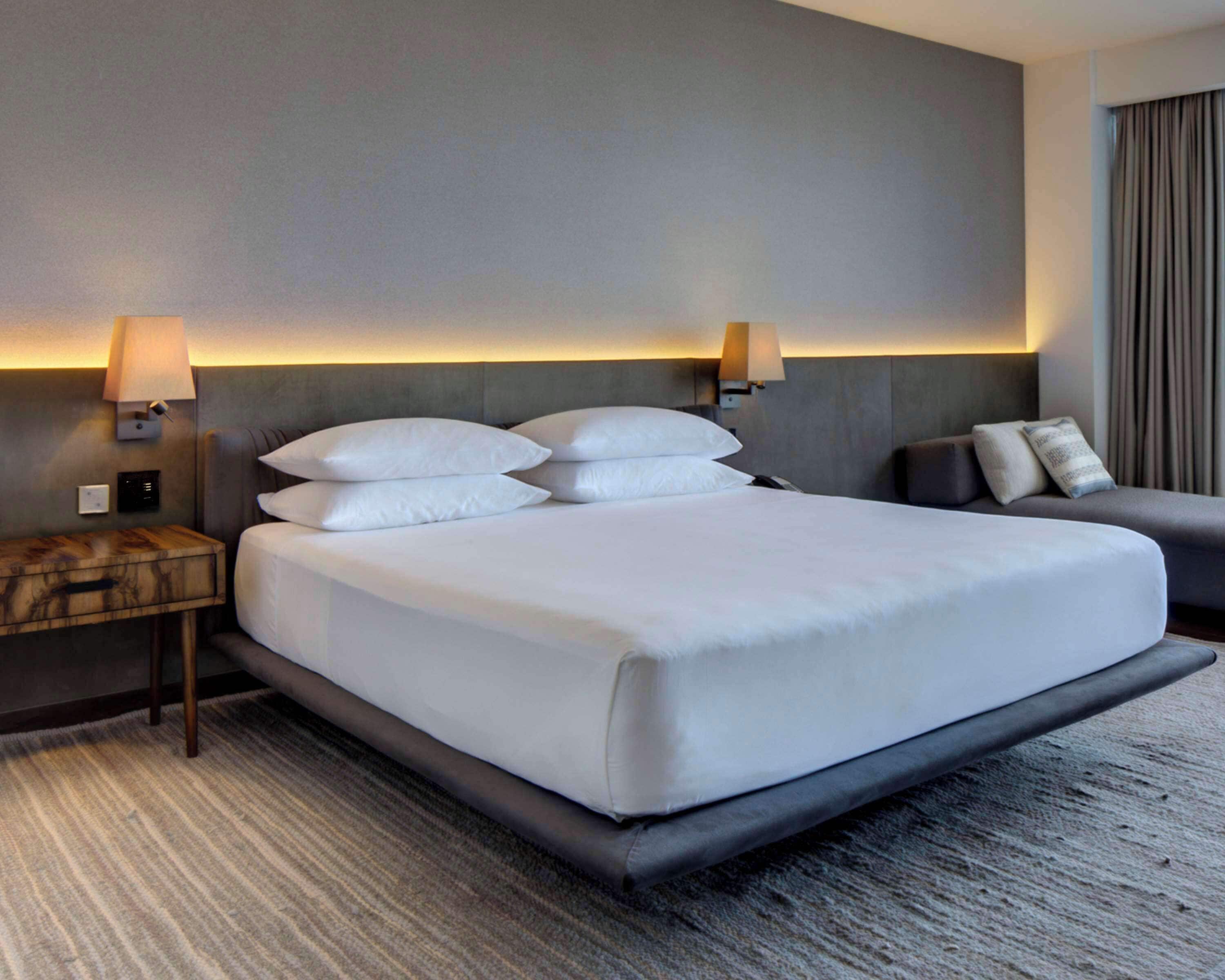 A hotel room with a large bed, two bedside tables, a sofa, and wall-mounted lamps.