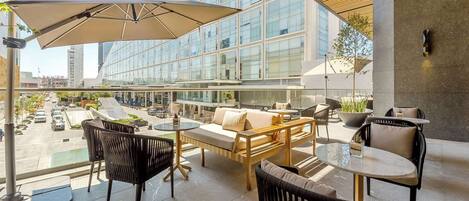 Un área de estar moderna al aire libre, con un gran paraguas, asientos cómodos y vistas de la ciudad.