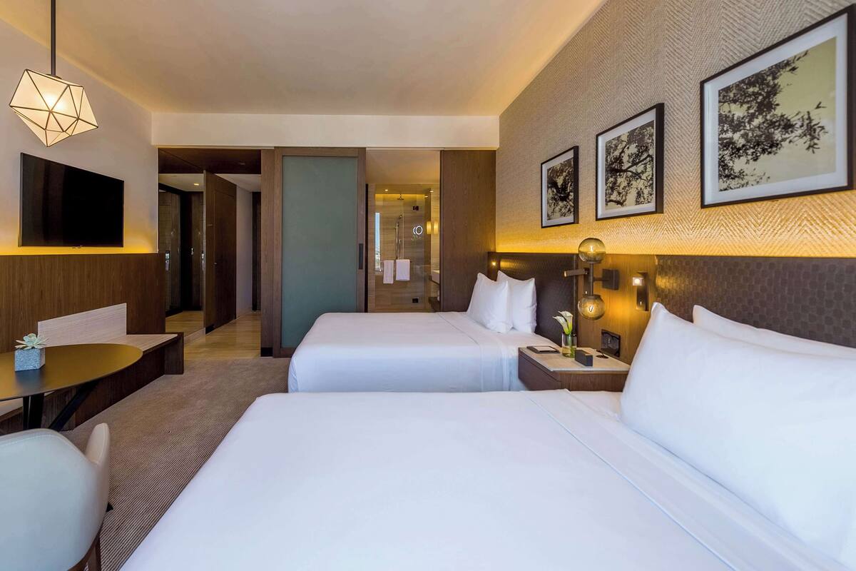 Une chambre d’hôtel avec deux lits, un bureau, une chaise, une télévision et des œuvres d’art accrochées au mur.