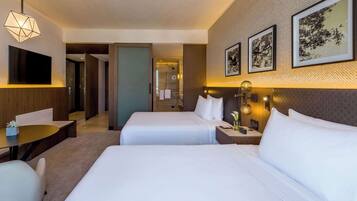 Habitación de hotel con dos camas, un escritorio, una silla, un televisor y obras de arte en la pared.