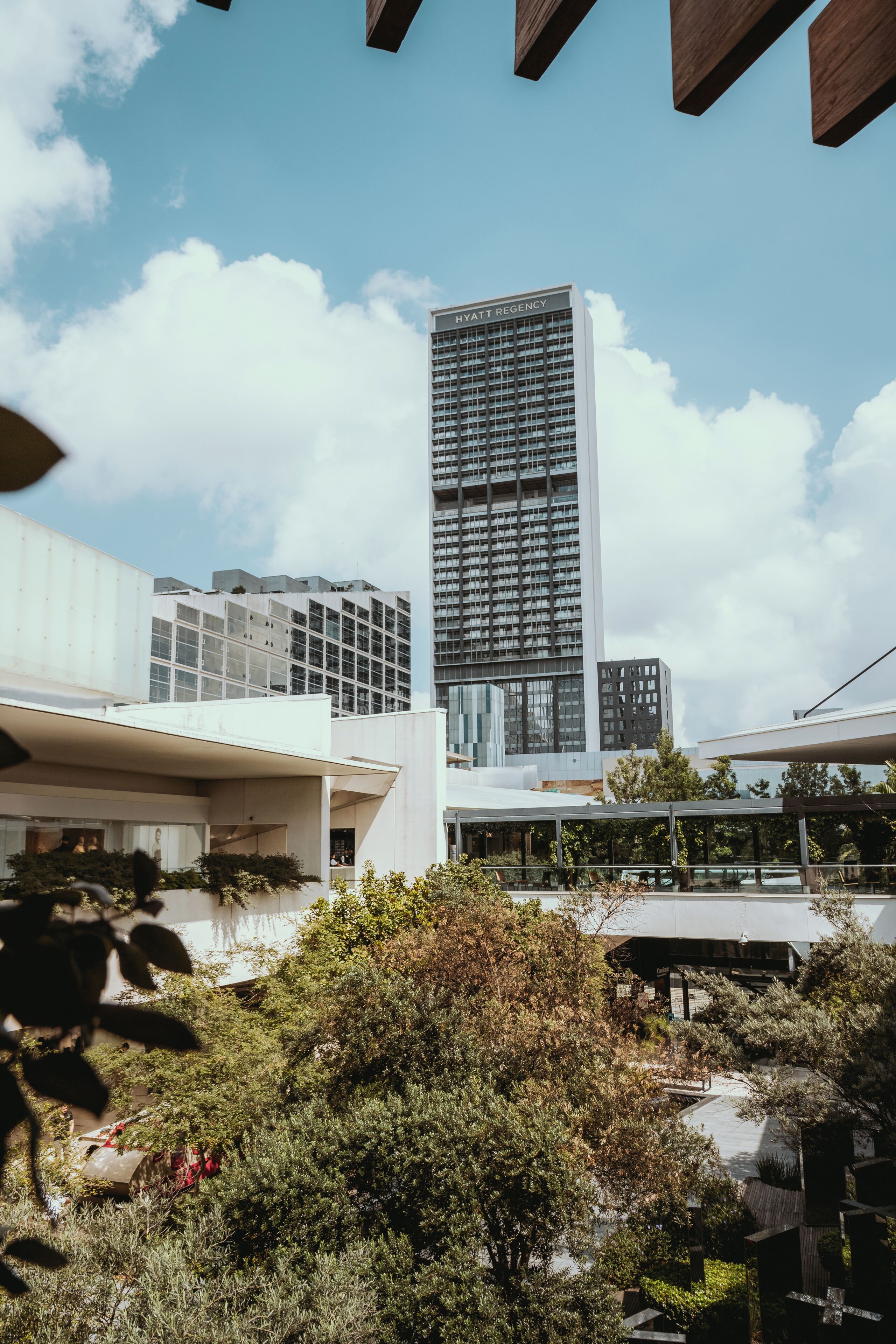A modern hotel with a prominent tower labeled "Hyatt Regency," surrounded by lush greenery and contemporary architecture.