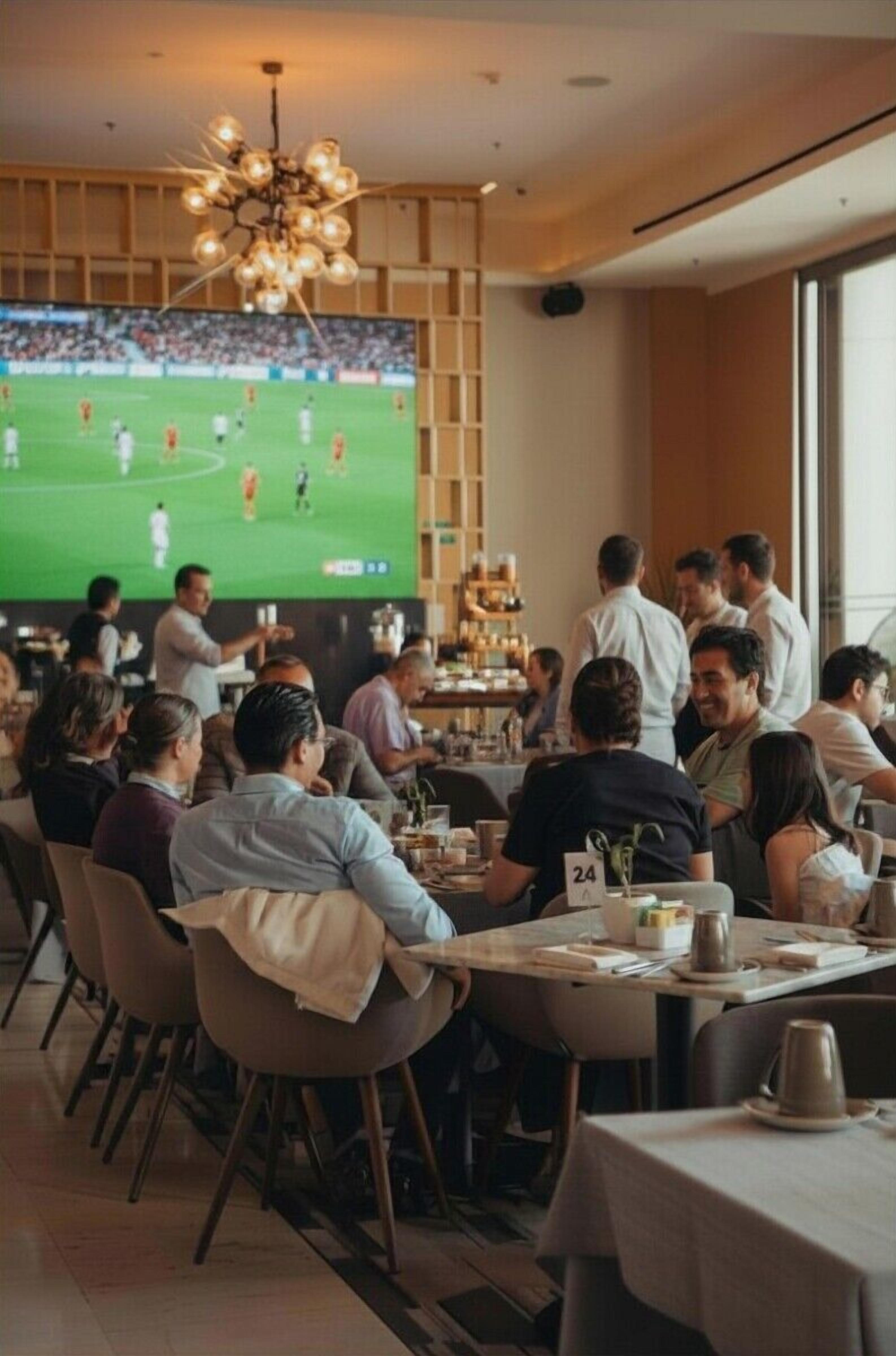 Un ristorante con un grande schermo televisivo che mostra un evento sportivo, pannelli in legno e un lampadario.