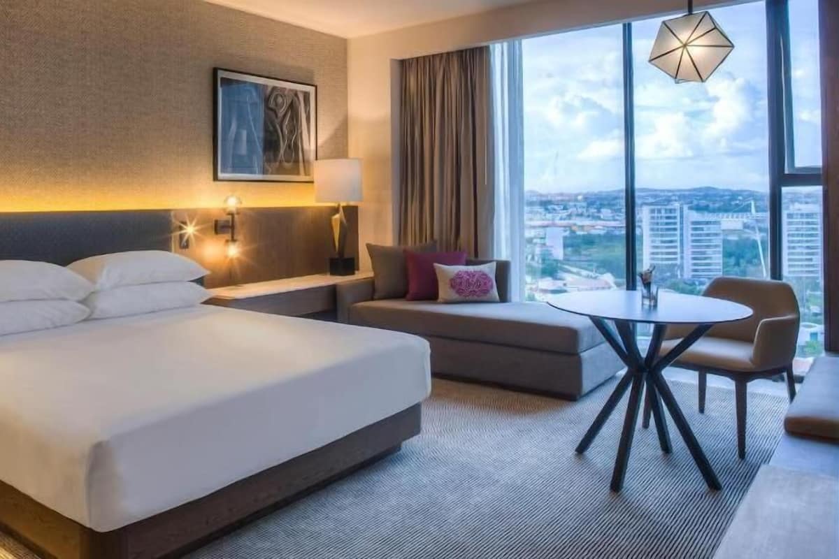 Une chambre d’hôtel avec un grand lit, un canapé, une petite table et une vue sur la ville.