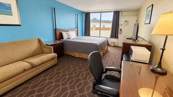 A hotel room with a bed, a sofa, a desk, a chair, a lamp, and a window with curtains.
