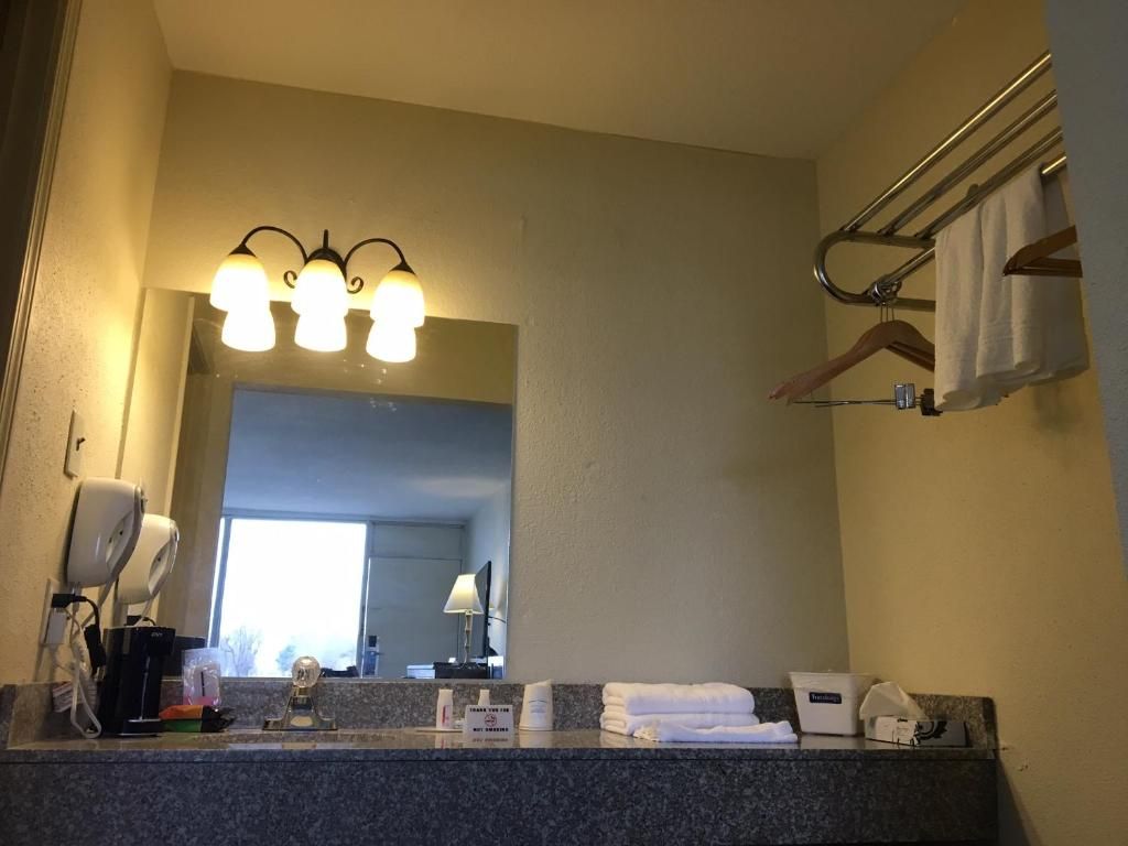 A hotel bathroom with a granite countertop, a mirror, a towel rack, and a coffee maker.