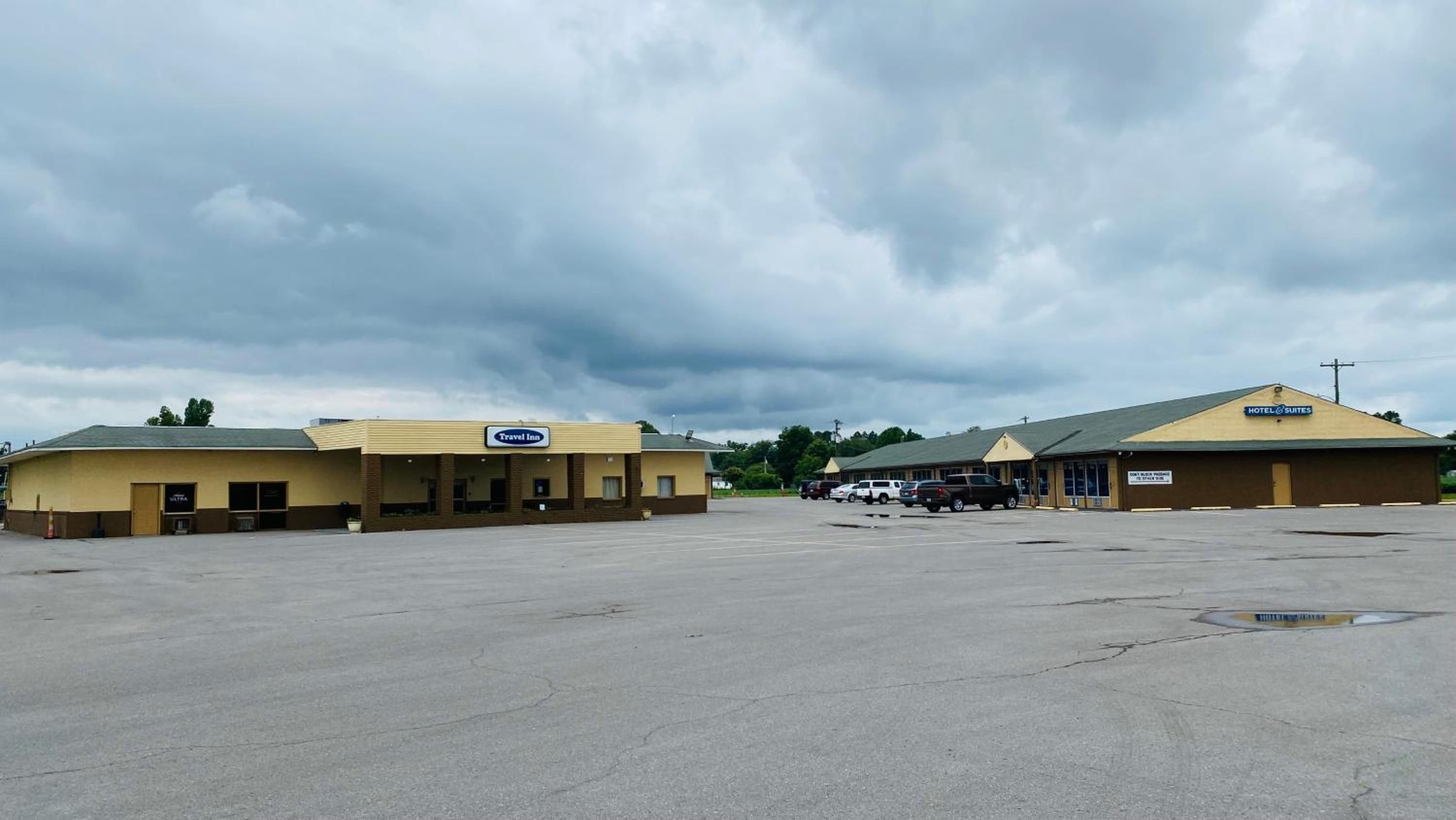 A Travel Inn and Hotel Suites with a large parking lot and a cloudy sky.