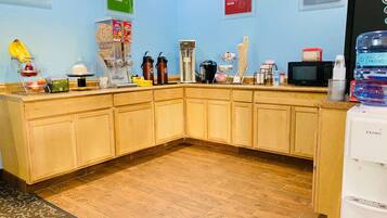 A kitchen with wooden cabinets, a coffee machine, a microwave, and various food items.