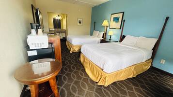 A hotel room with two beds, a desk, a chair, a mirror, a lamp, and a picture on the wall.