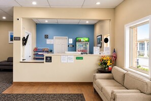 A reception area with a counter, a refrigerator stocked with beverages, a no smoking sign, and a window with an American flag. - Travel Inn Marston I-55 by Hotel O (Marston)