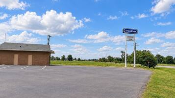 A Travel Inn with a sign indicating affordable rooms, a parking lot, and a clear sky.
