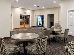 A hotel lobby with a glass table and checkered chairs, an exit door, and a vending machine. - Travel Inn Marston I-55 by Hotel O (Marston)