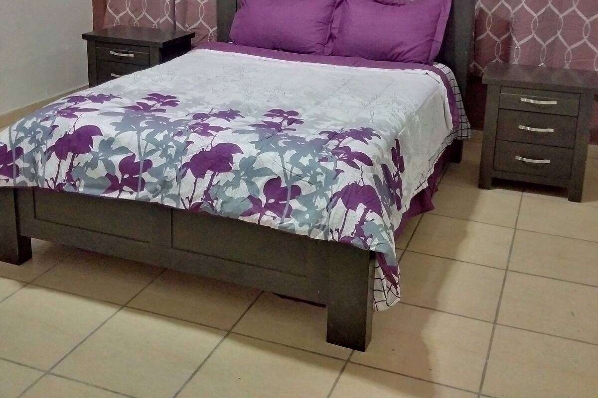 A bed with a floral bedspread, two nightstands, and a headboard with a headboard panel.