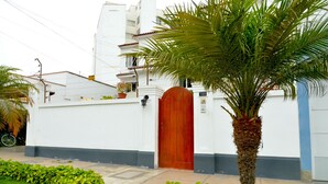 A white building with a red door, a palm tree, and a bicycle parked outside. - Residencial Carlos (Lima)
