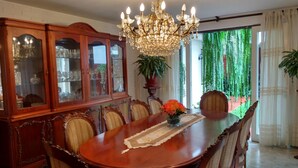 A dining room with a large wooden table, ornate chairs, a chandelier, and a view of greenery outside. - Residencial Carlos (Lima)