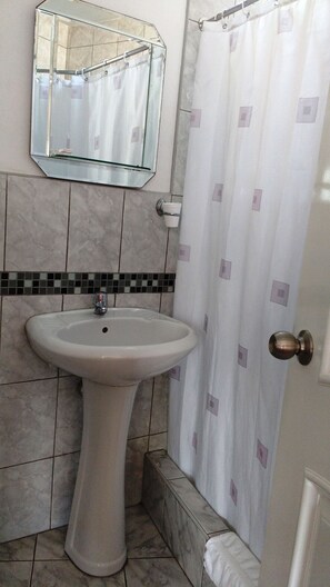 A bathroom with a pedestal sink, a mirror, a shower curtain, and tiled walls. - Residencial Carlos (Lima)