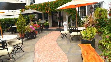 An outdoor patio area with tables and chairs, surrounded by potted plants and flowers.