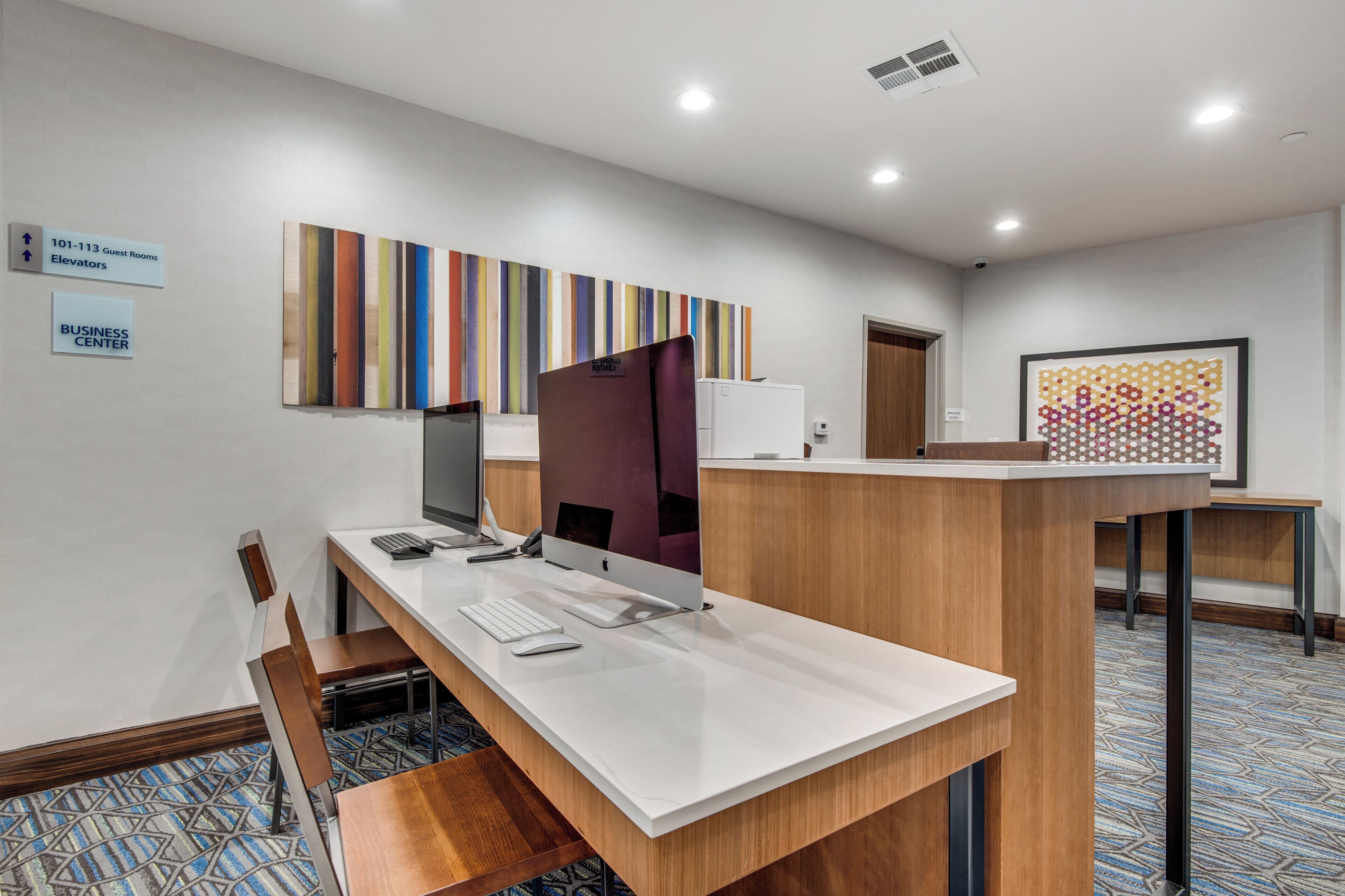 A hotel reception desk with a computer, a telephone, and a seating area with a chair. There are signs indicating guest rooms and a business center.