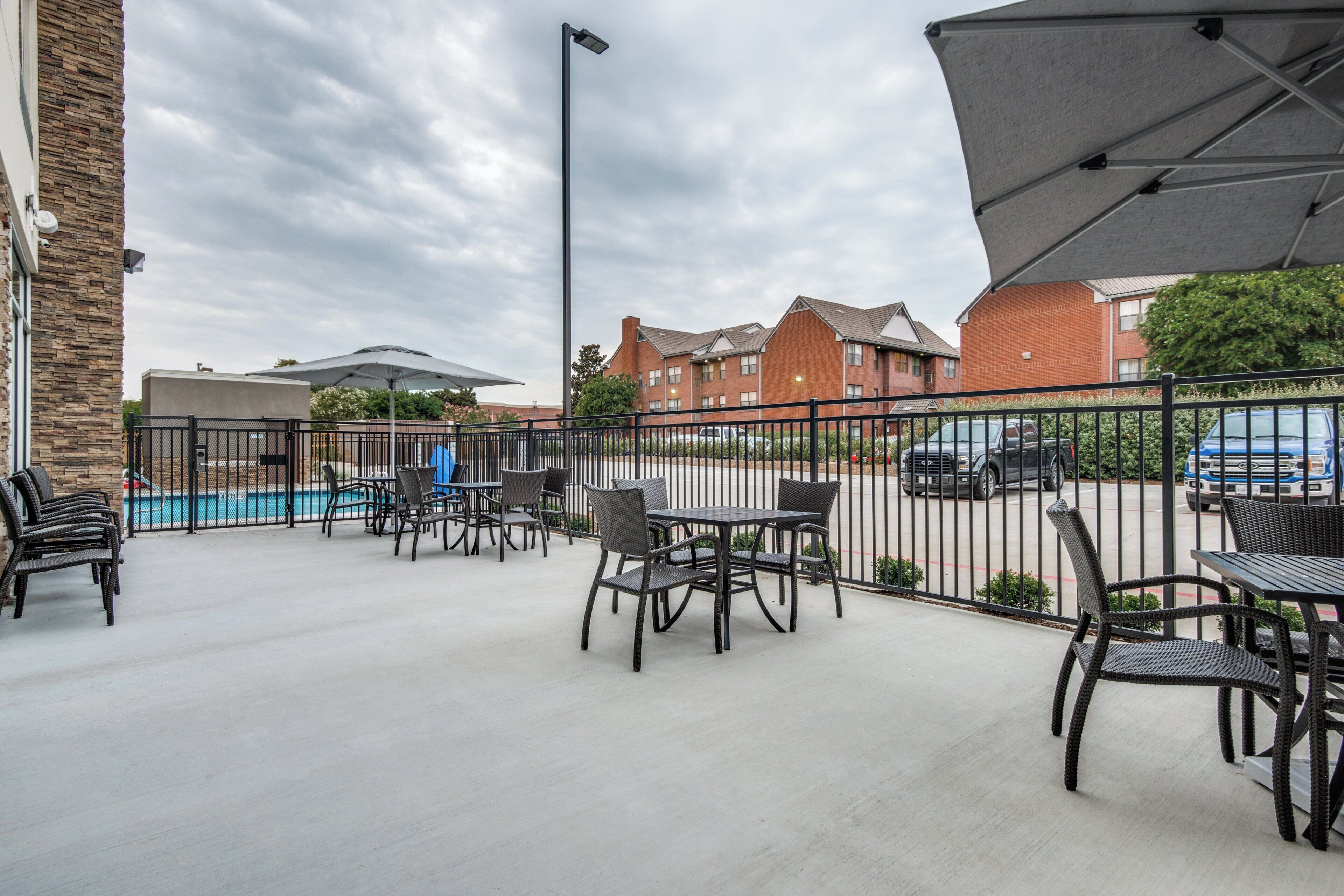 An outdoor patio area with tables and chairs, a pool, and a parking lot in the background.