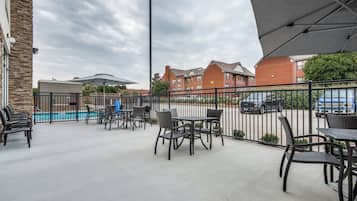 An outdoor patio area with tables and chairs, a pool, and a parking lot in the background.