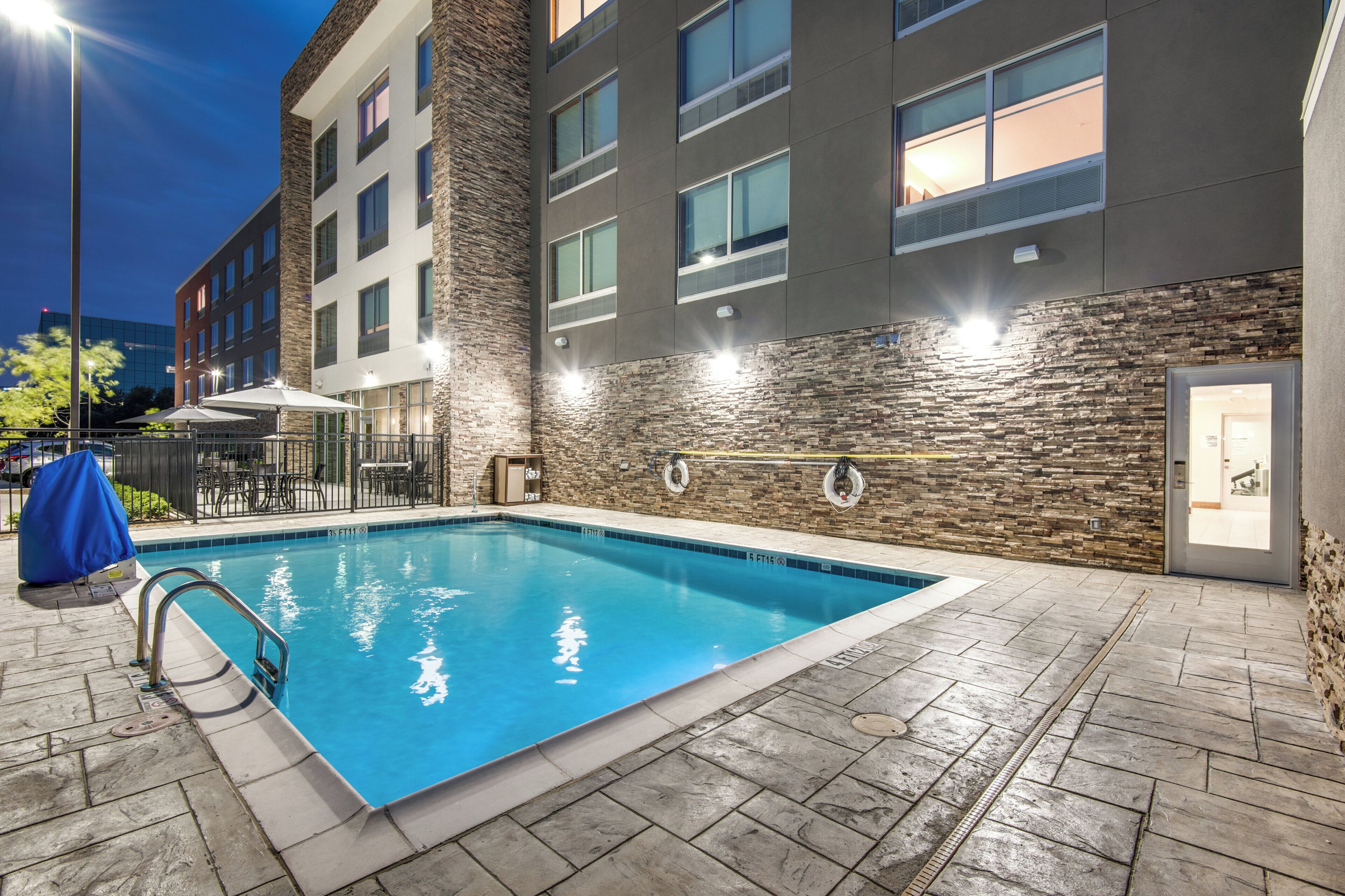 Una piscina con un muro de piedra, una zona de estar cubierta y un edificio con varias ventanas.