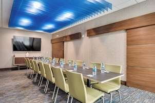 A conference room with a long table, chairs, water bottles, and a television on the wall.