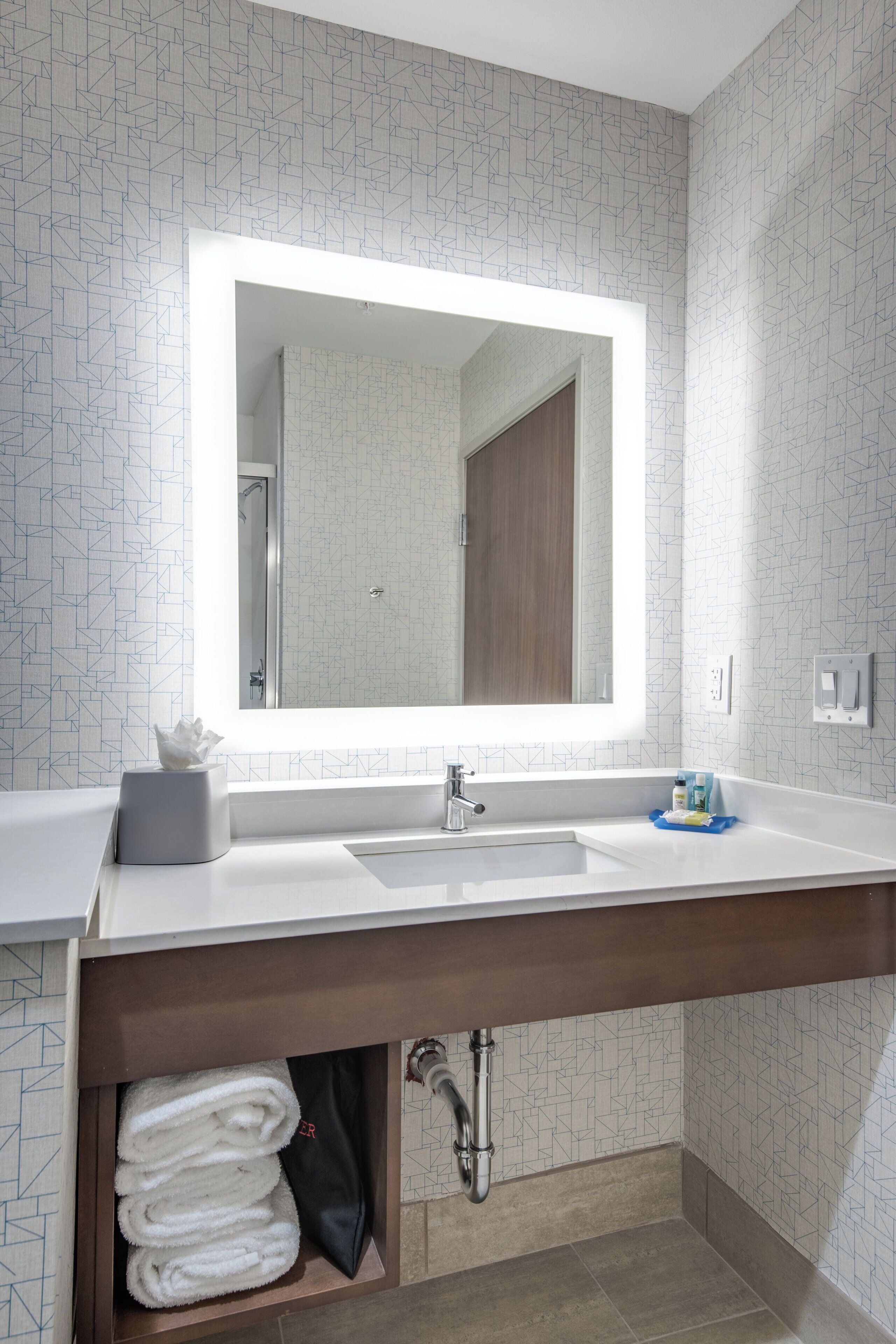 A modern bathroom with a large mirror, white sink, and a towel rack under the counter.