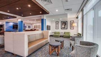 A hotel lobby with a seating area, a reception desk, and a large window.
