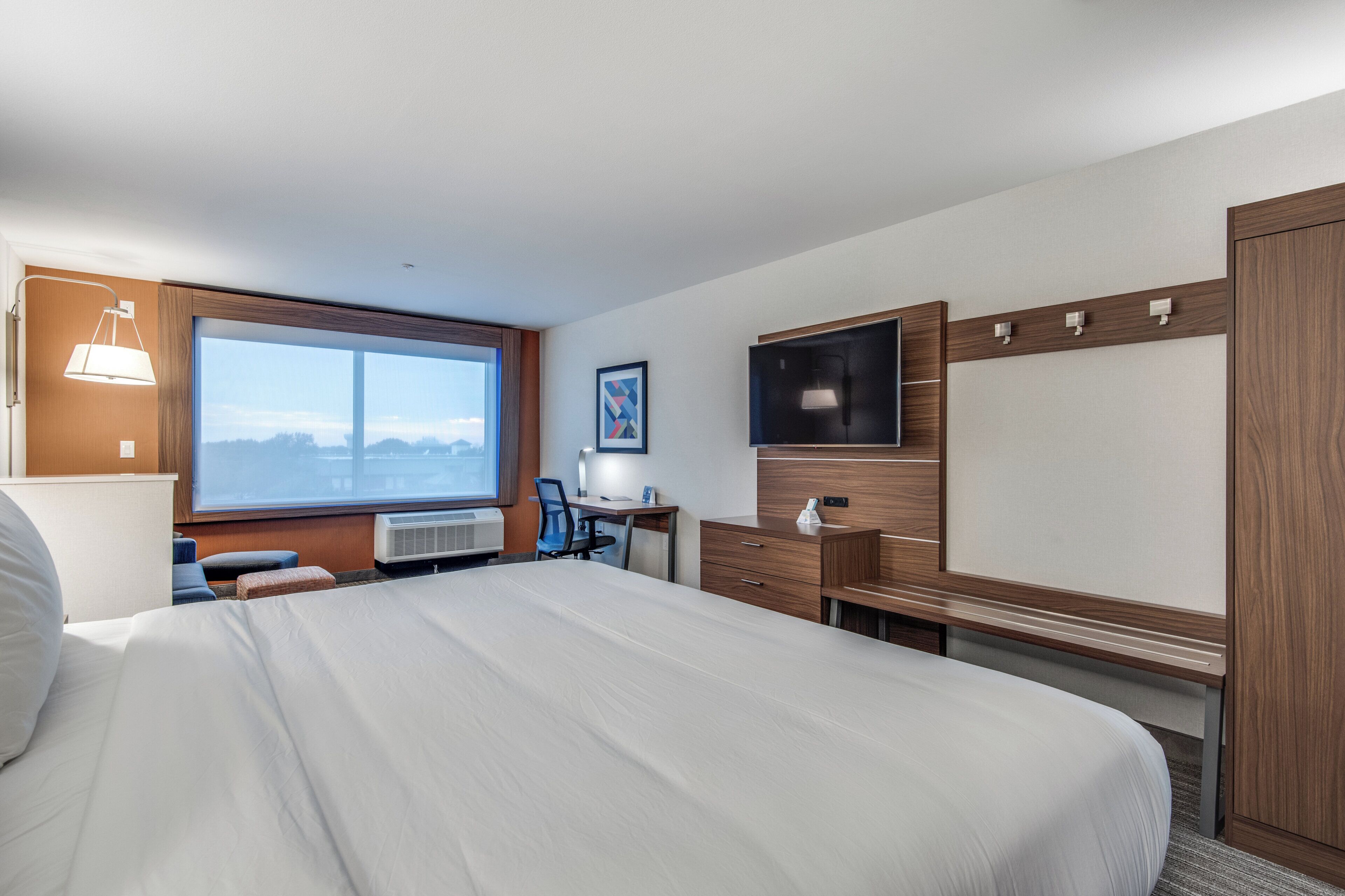 A hotel room with a large bed, a desk with a chair, a TV, and a window with a view.