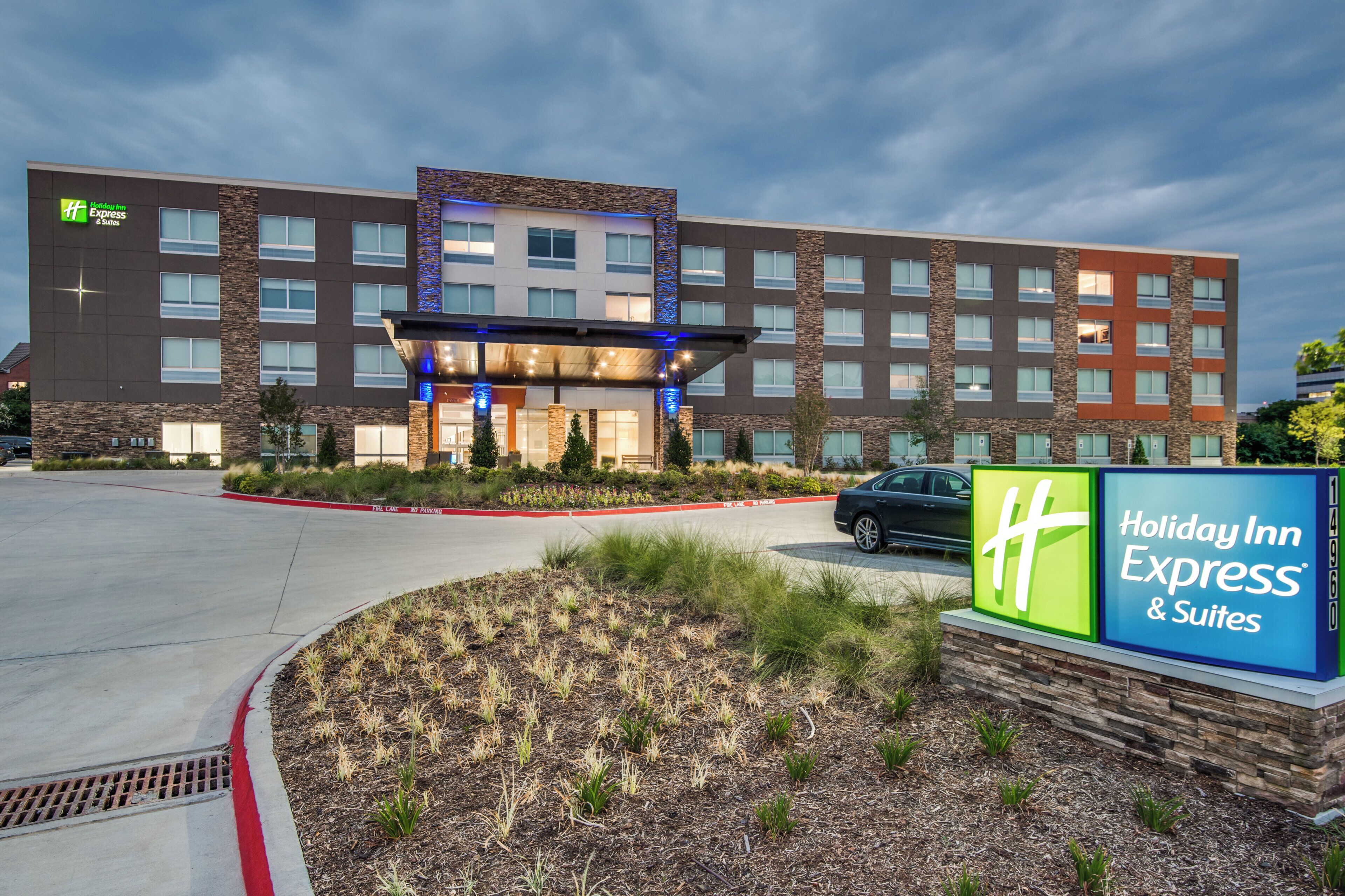 A Holiday Inn Express & Suites building with a modern design, featuring a prominent entrance and a landscaped area in front.
