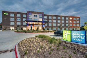 A Holiday Inn Express & Suites building with a modern design, featuring a prominent entrance and a landscaped area in front.