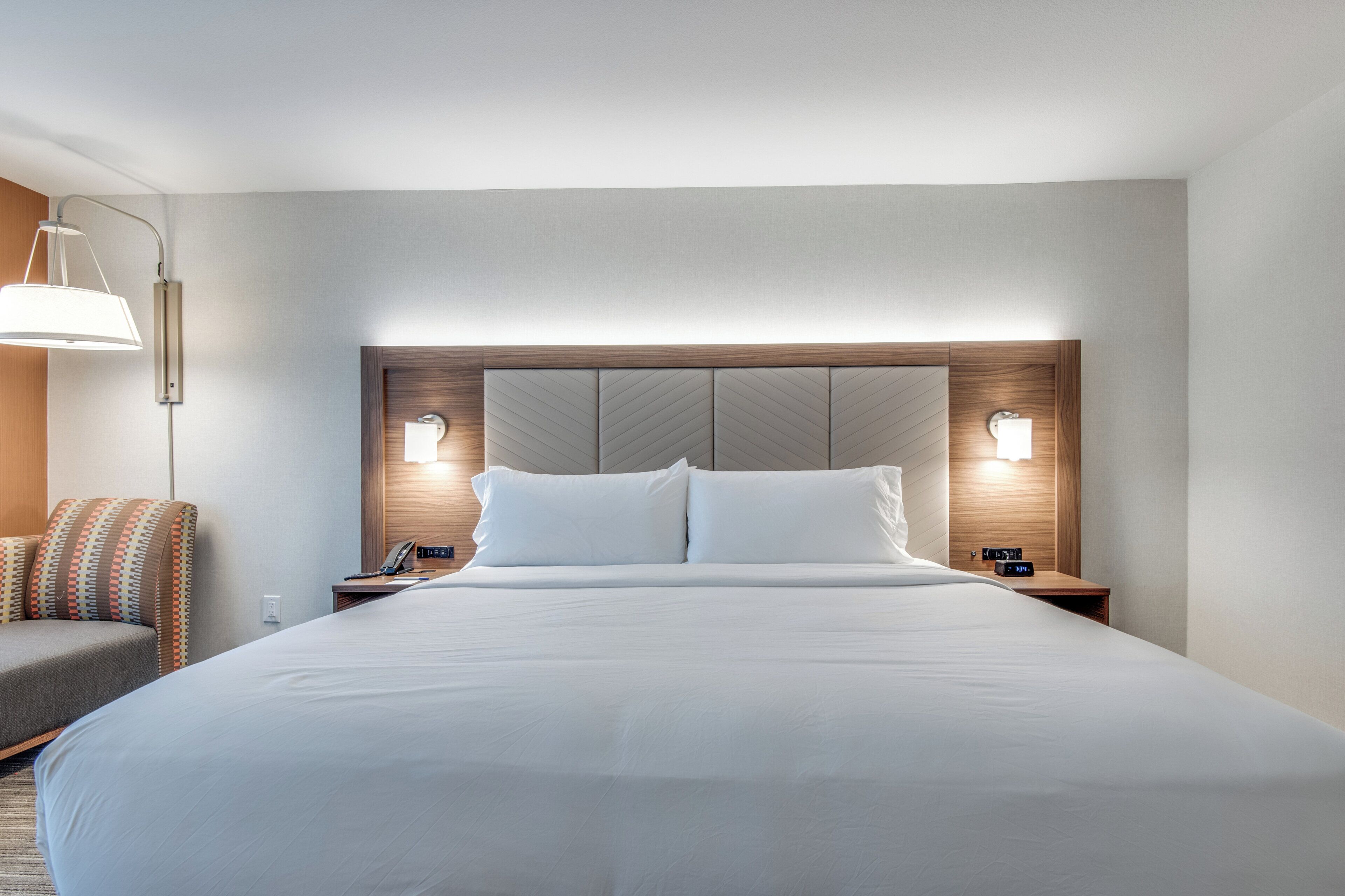 Una habitación de hotel con una cama grande, dos mesitas de noche, una lámpara y una silla.