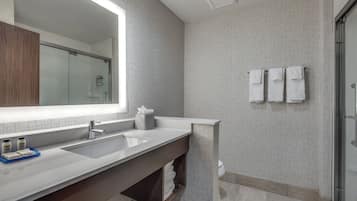 A modern bathroom with a large mirror, two sinks, a towel rack, and a shower area.