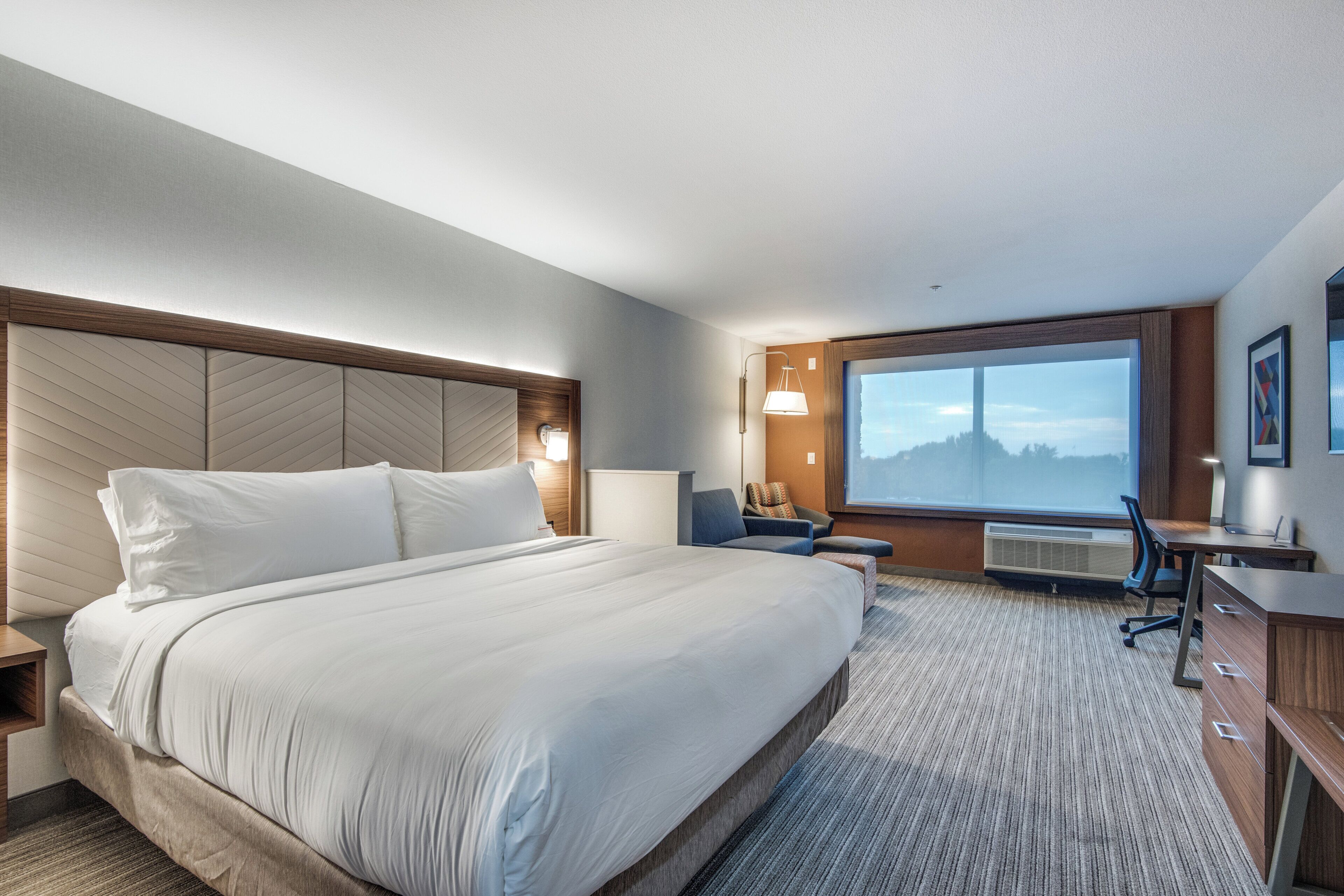 Habitación de hotel con una cama grande, un escritorio, una silla y un ventanal con vistas.