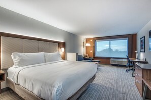 A hotel room with a large bed, a desk, a chair, and a large window with a view. - Holiday Inn Express & Suites Dallas North - Addison by IHG (Dallas)