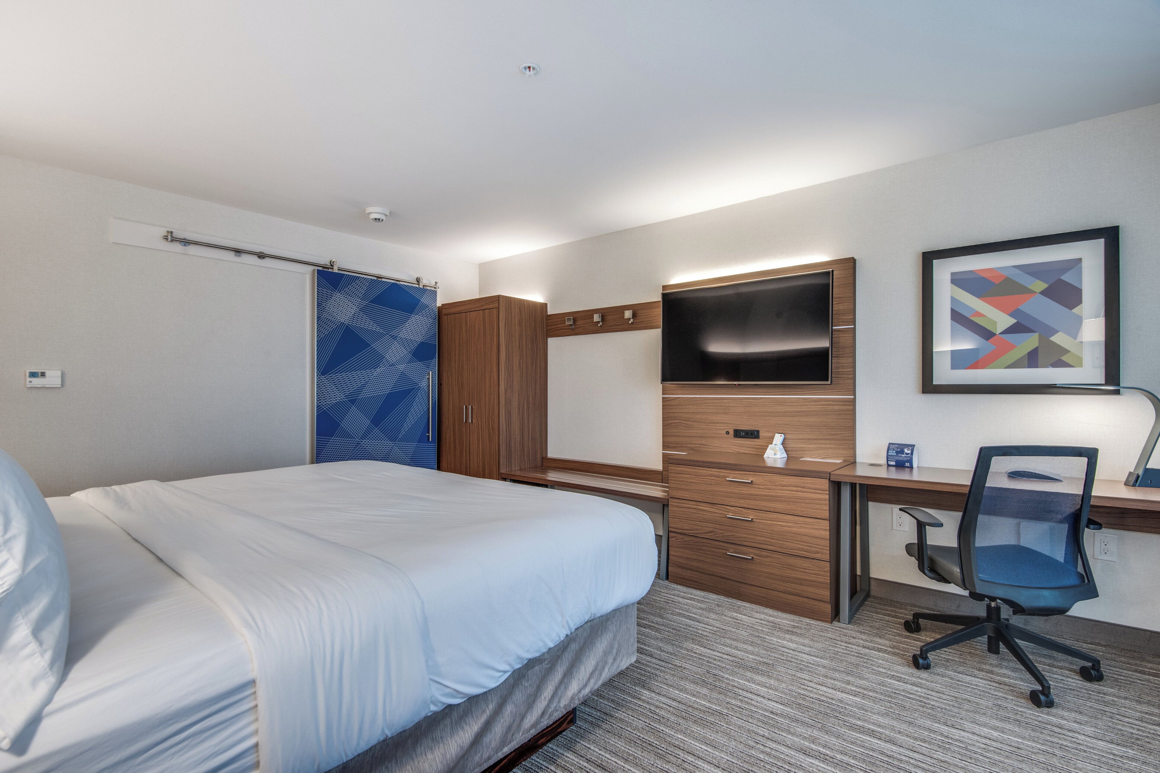 A hotel room with a bed, a desk, a chair, a TV, and a wardrobe.