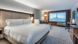 A hotel room with a large bed, a desk, a chair, and a large window with a view of a cityscape. - Holiday Inn Express & Suites Dallas North - Addison by IHG (Dallas)