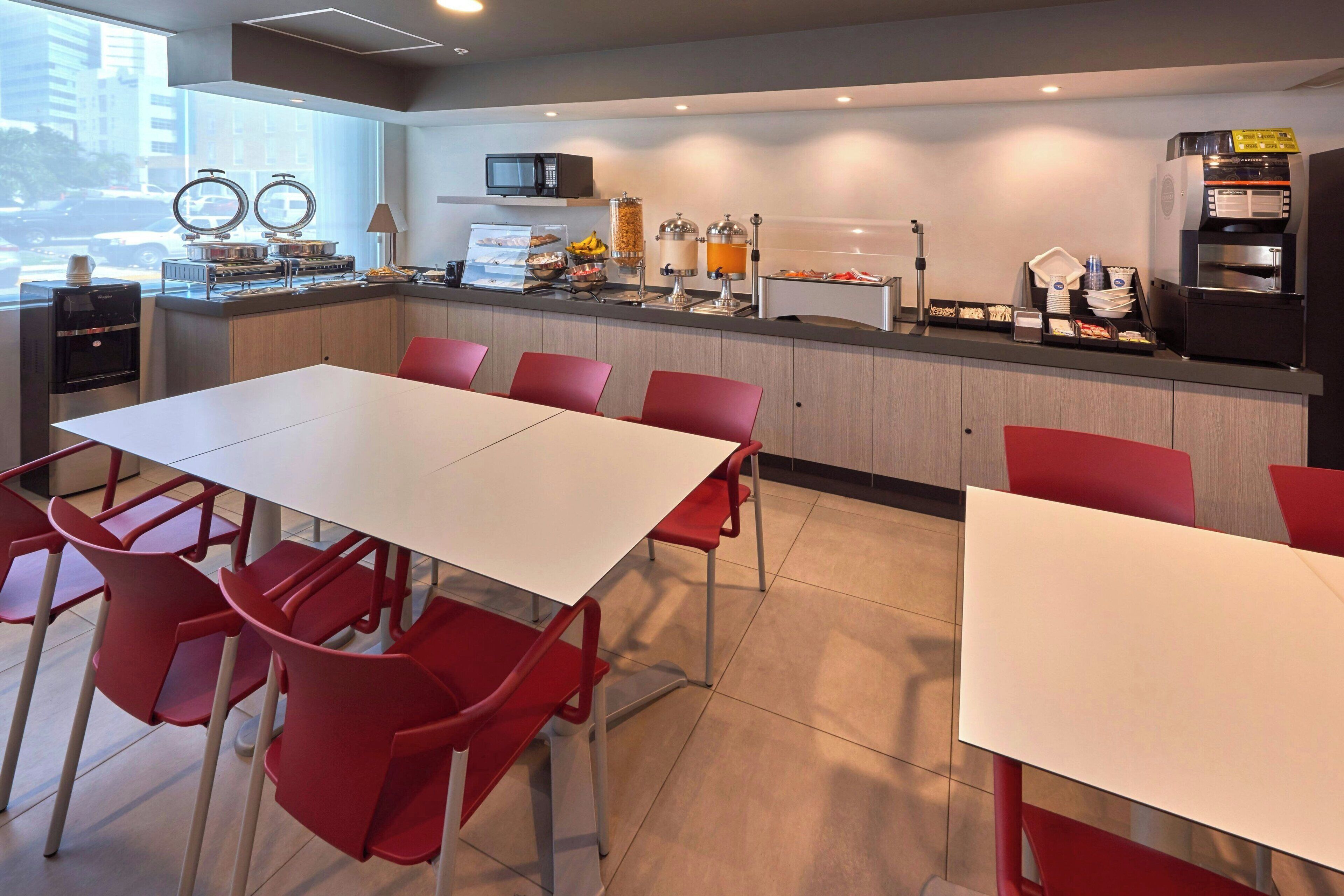 A modern kitchen with a white countertop, red chairs, and a large window.
