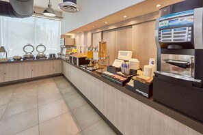 A hotel breakfast area with a long counter, various food items, a coffee machine, and a self-service beverage dispenser. - City Express Junior by Marriott Toluca Zona Industrial (Toluca)