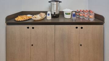A kitchenette with a coffee maker, a bowl of cookies, a water dispenser, and several water bottles.